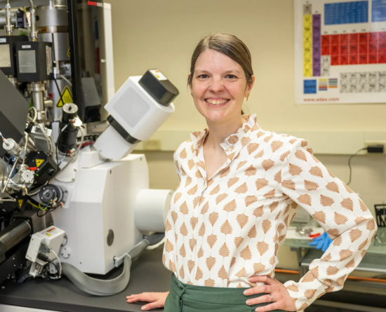 Amanda Krause standing at microscopy machine with periodic table in background